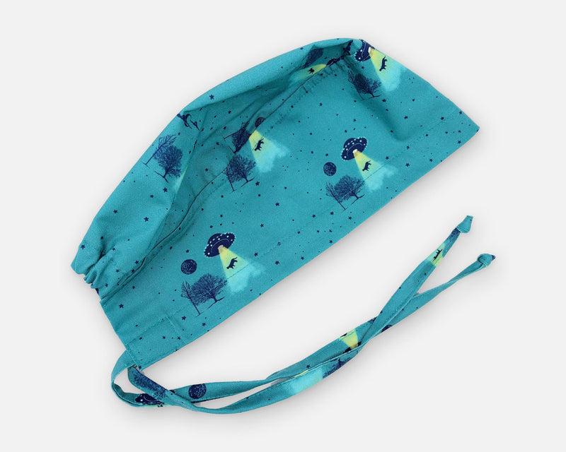 Teal cotton surgical scrub cap with UFOs, yellow light beams, trees and animal silhouettes, shown diagonally with matching fabric ties.