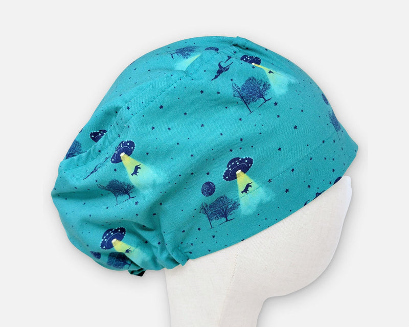 Teal cotton Euro scrub cap with UFOs, yellow light beams, trees and animal silhouettes, shown in profile on a fabric mannequin.