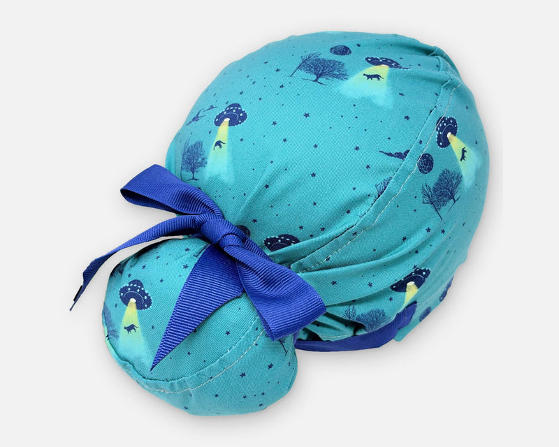 Teal cotton Euro Plus scrub cap with UFOs, yellow beams and trees, shown from the rear three-quarter angle with a royal blue ribbon bow.