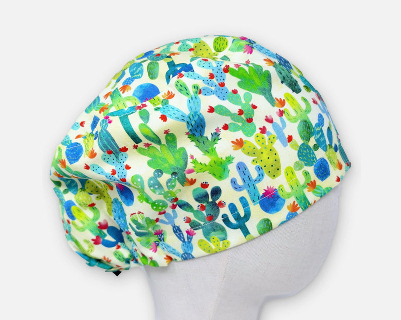 Cream cactus print Euro scrub cap on a mannequin, shown in side profile against a light gray background. Green, blue and turquoise cacti have colorful flowers.